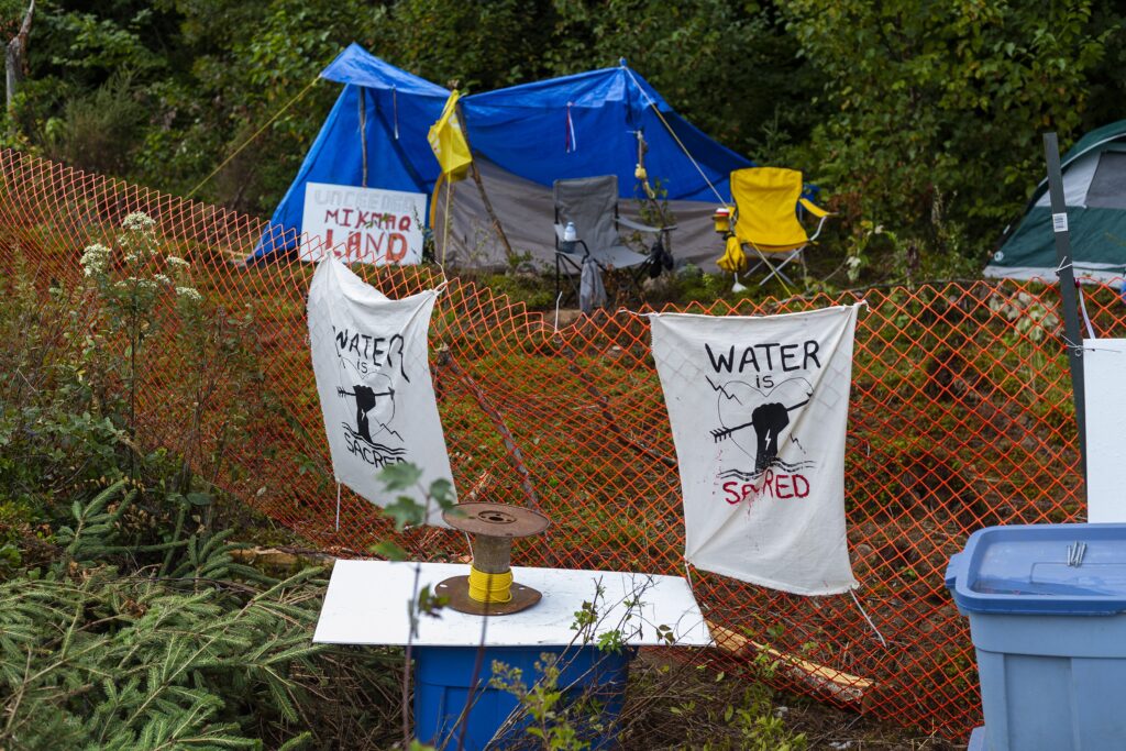 标志贴在橙色的雪栅栏上，挡住了一片树林。篱笆后面是帐篷和椅子。今天是阴天。