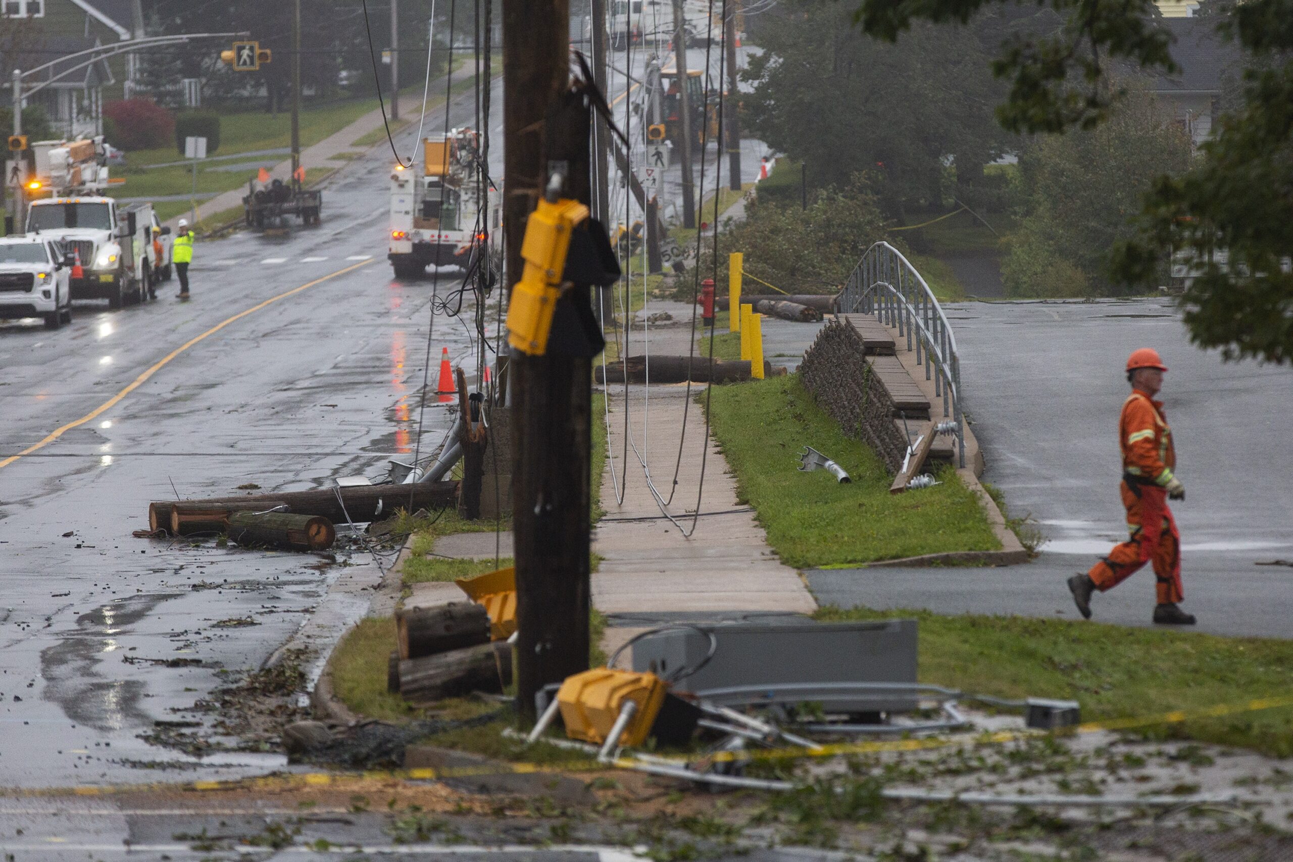 一个穿橙色衣服的工人走出街道，从画面中走出来。到处都是电线和碎片。