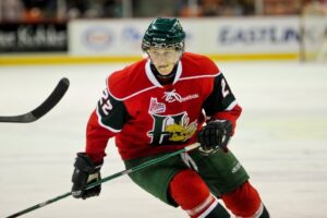 一名曲棍球运动员穿着红色的驼鹿头(Mooseheads)制服，独自滑过蓝色线，背景是冰和滑板。