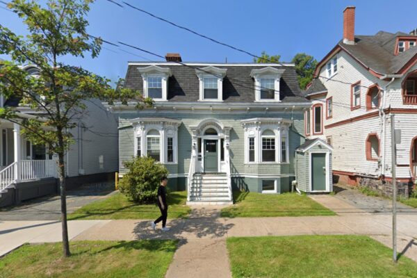 在一个阳光明媚的日子里，我们可以看到一座绿色的老房子，人行道上有一个行人走过。