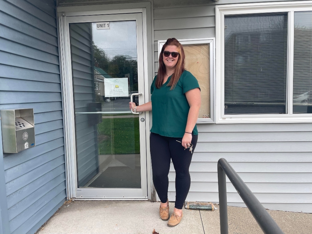 一个红色长发的女人，身穿绿色上衣，深色裤子，米色鞋子，站在一户人家的门口。