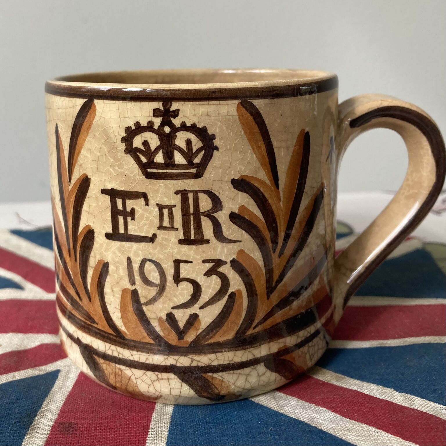 陶器马克杯显示一个皇冠上面的字母E II R和1953，以及一个程式化的月桂装饰。马克杯上印着英国国旗。