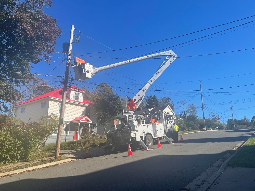 在一个阳光明媚的日子里，一名电线工人坐在一辆公用卡车的铲斗里，在一条多山的街道上修理电线。