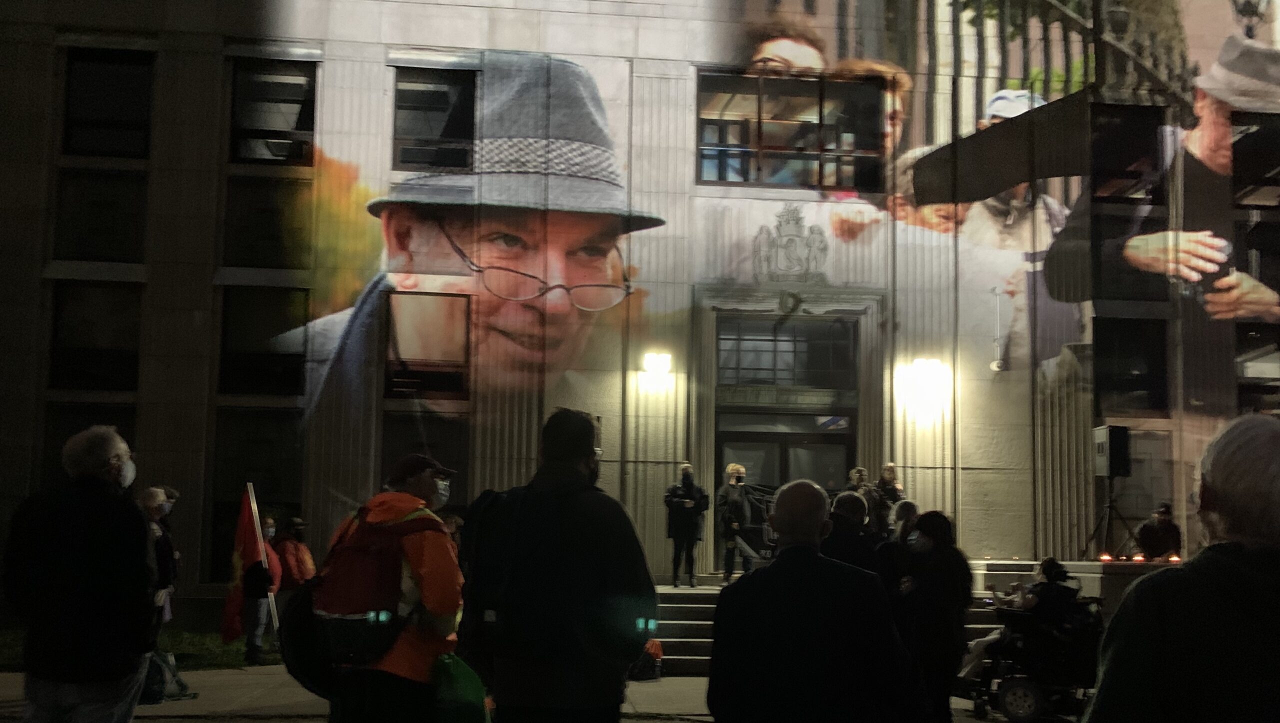 Robert Devet纪念馆的一张照片，显示Robert的照片投射在位于春天花园路的旧纪念图书馆的前面。人群聚集在外面，一些人站在旧图书馆的台阶上。